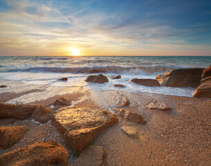 Stones and sea during the sunset. Beach shore among rocks and stones on evening sunset.