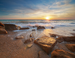 Stones and sea during the sunset. Beach shore among rocks and stones on evening sunset.