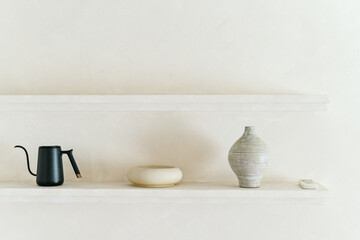 Minimalist decor with black kettle, beige bowl, and striped vase on shelf