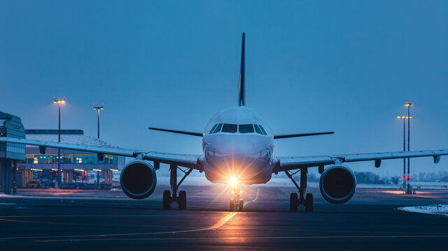 Traffic at airport at night. Front view of passenger airplane taxiing to runway for taking off..