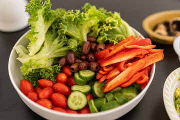 A bowl filled with fresh greens, red bell peppers, cherry tomatoes, cucumbers, and olives showcases a healthy salad ready to be enjoyed at a gathering or meal time.