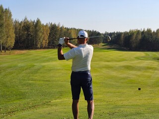 Golfer preparing to swing on a sunny day on a lush green course surrounded by trees