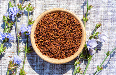 Ground chicory root in a wooden cup and chicory flowers on a rustic wooden background. Alternative medicine. Healthy drinks. chicory drink