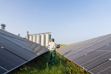 Female farmer with digital tablet on a modern farm using solar panels. Agricultural silos in the...