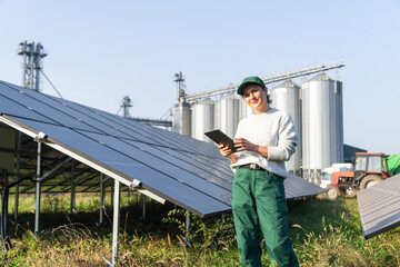 Female farmer with digital tablet on a modern farm using solar panels. Agricultural silos in the...