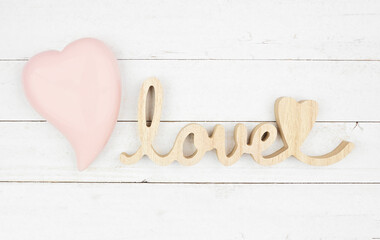 Valentines Day theme wooden love text with pink glass heart. Top down view over a rustic white wood background.