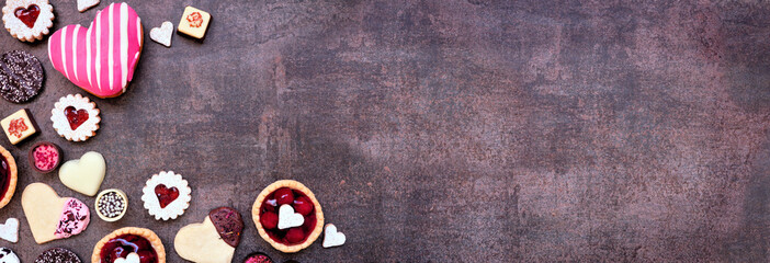 Valentines Day baking and sweets corner border with a variety of cookies, chocolates and sweet treats. Top view on a dark stone banner background with copy space. Love and hearts theme.