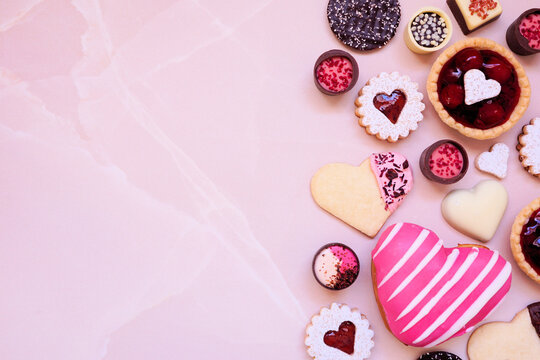 Valentines Day baking and desserts side border with a variety of cookies, chocolates and sweet treats. Above view on a pink stone background with copy space. Love and hearts theme.