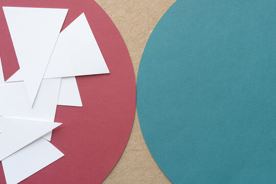 pile of white paper isosceles triangles on a red geometric form and part of a green paper circle on brown