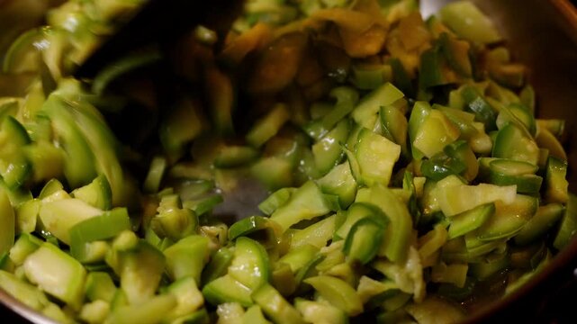 plan fixe vid&eacute;o de cuisine, m&eacute;lange de la po&ecirc;l&eacute;e de l&eacute;gumes, dans une po&ecirc;le inox, les jolies courgettes vertes durant la cuisson sont remu&eacute;es &agrave; l'aide d'un ustensile de cuisine