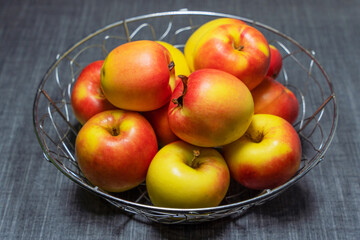 There are beautiful fresh red and yellow apples in a metal vase on a gray table.