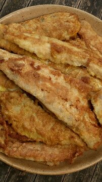 A pile of fried pike-perch fillets coated in flour and egg on a plate. Top view, table spin. Vertical video.