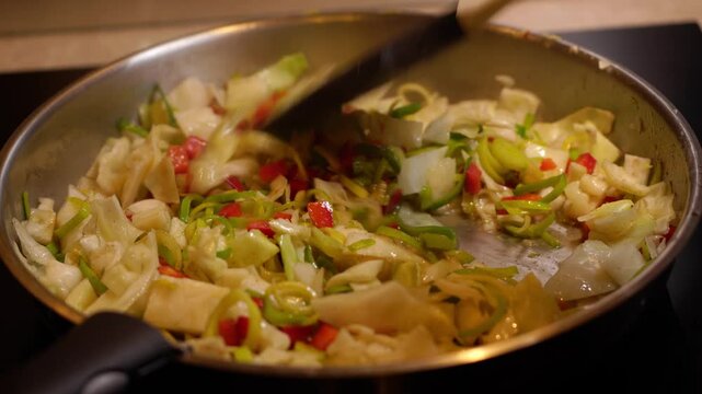 plan fixe vid&eacute;o avec remuage de l&eacute;gumes vari&eacute;s, dans une po&ecirc;le inox, &agrave; l'aide d'une spatule noire en Silicon 