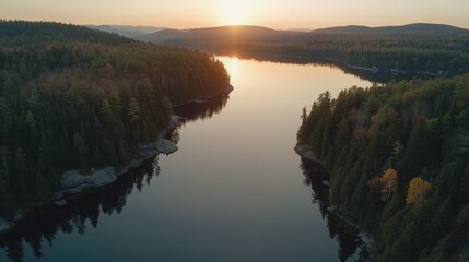 Fototapeta premium Sunset over calm lake nestled in forest, aerial view.