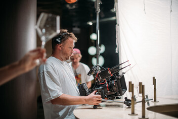 Director of photography with a camera in his hands on the set. Professional videographer at work on filming a movie, commercial or TV series. Filming process indoors, studio