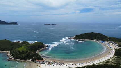 Aerial drone view of Conchas Beach (praia), Cabo Frio, Rio de Janeiro, Brazil. The beach’s unique shell-like shape stands out, surrounded by clear Atlantic Ocean waters and stunning natural scenery.