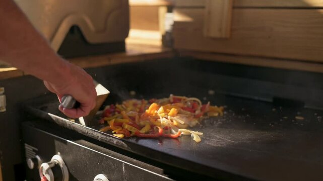 Cooking Colorful Vegetables on Outdoor Griddle Close-up of vibrant vegetables being cooked outdoor griddle hand holding spatula stirs sizzling, fresh ingredients under natural light.
