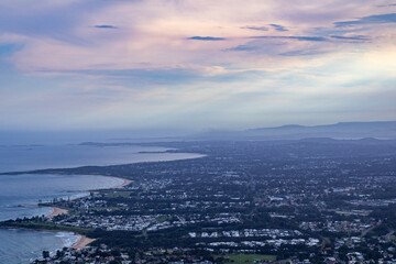 Obraz premium A scenic aerial view of a coastal city nestled along the shoreline. The city meets the ocean, with beaches, cliffs, and urban development visible. Rolling hills or mountains are visible in the distanc