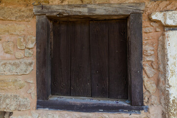A dark, weathered wooden shutter covers a window opening in a rough stone wall.
