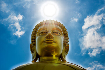 Złoty Budda w promieniach słońca na tle błękitnego nieba – symbol duchowego oświecenia i harmonii © damian