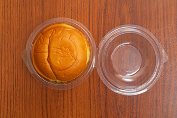 Delicious butter bun in clear plastic packaging on a wooden table surface