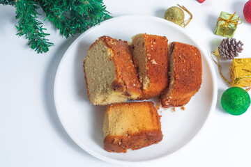 Top view of festive cake slices on white plate with Christmas ornaments and pine branch on white background
