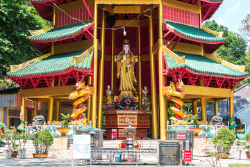 Złota figura Guanyin w wielobarwnej pagodzie otoczonej smokami i tropikalną zielenią – harmonia duchowości i tradycji azjatyckiej © damian