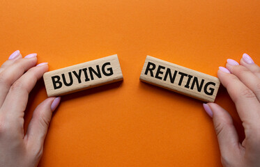 Buying or Renting symbol. Concept word Buying or Renting on wooden blocks. Businessman hand. Beautiful orange background. Business and Buying or Renting concept. Copy space