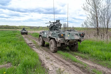 Military vehicles maneuver through grassy terrain during a training exercise in rural area