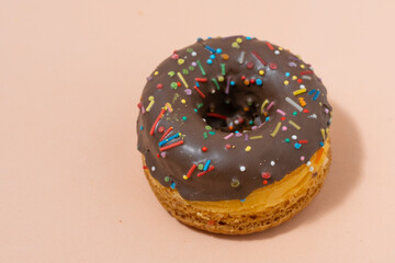 Donut with chocolate glaze and multicolored sprinkles on beige background.