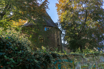 Behind a high ivy-covered wall you can see a historic building surrounded by trees and bushes