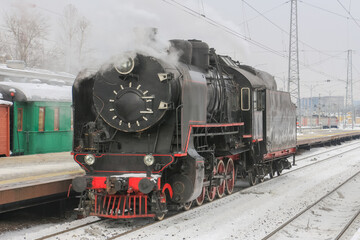 An old steam locomotive in clouds of smoke near a railway station platform