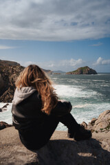 A woman sits overlooking Galician cliffs and islands, perfect for travel and solitude themes.