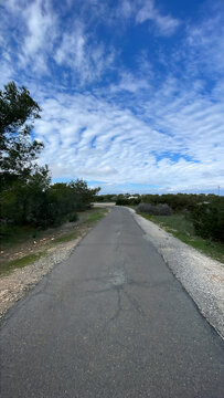 Curving Asphalt Road Through Lush Greenery Under a Bright Blue Sky with Soft White Clouds in a Peaceful Countryside Setting