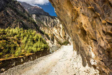 Deep narrow Marsyangdu river gorge near Bhratang village and the gravel road hacked in a stone. Around Annapurna trek, Nepal.