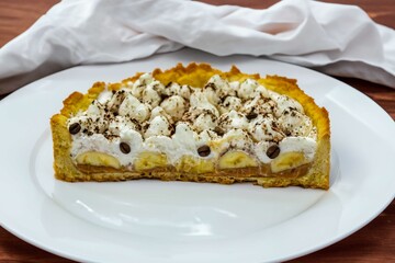 Authentic banoffee cake with banana and caramel sauce filling sprinkled with grated dark chocolate and coffee . English traditional pie