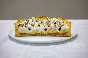 Authentic banoffee cake with banana and caramel sauce filling sprinkled with grated dark chocolate and coffee . English traditional pie