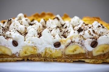 Authentic banoffee cake with banana and caramel sauce filling sprinkled with grated dark chocolate and coffee . English traditional pie