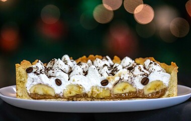 Authentic banoffee cake with banana and caramel sauce filling sprinkled with grated dark chocolate and coffee . English traditional pie