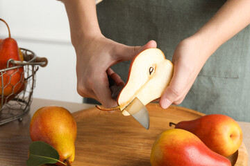 Woman cutting ripe juicy pear at table, closeup