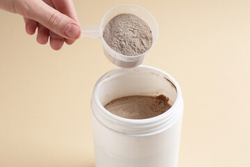 Woman taking scoop of protein from jar on beige background, closeup