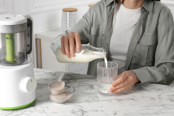 Making protein cocktail. Woman pouring milk from bottle into glass at white marble table, closeup