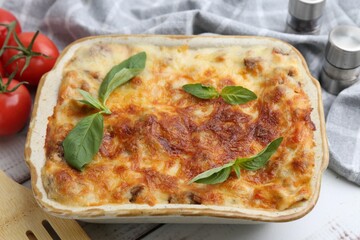 Delicious cooked lasagna in baking dish and basil on table, closeup
