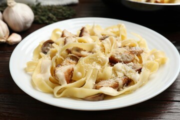 Tasty Alfredo pasta with chicken and mushrooms on wooden table, closeup