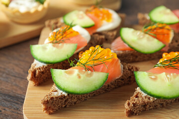 Tasty canapes with salmon and cucumber on wooden table, closeup