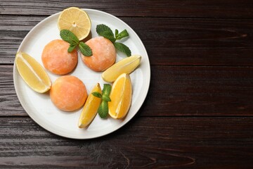 Plate with tasty mochi, cut orange, lemon and mint on wooden table, top view. Space for text