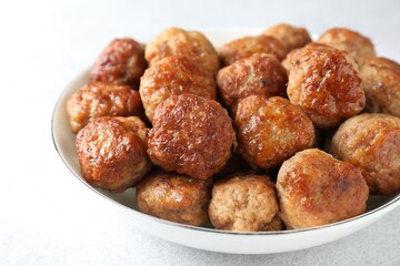 Tasty cooked meatballs in bowl on white table, closeup