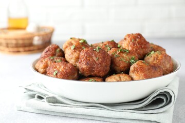Tasty cooked meatballs with green onion in bowl on white table, closeup