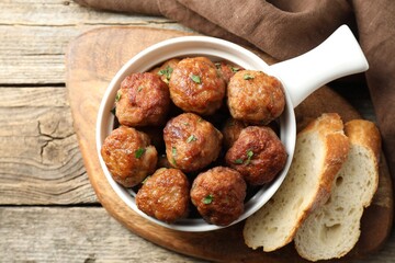 Tasty meatballs with green onion in baking dish and bread pieces on wooden table, flat lay