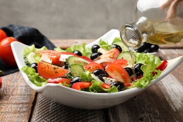 Adding olive oil to Greek salad at wooden table, closeup